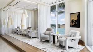 A modern living room with a view of the water, featuring a sofa set, pendant lights, and a large window with curtains.