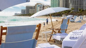 Beach chairs with towels, umbrellas, and a view of the ocean and buildings in the background.