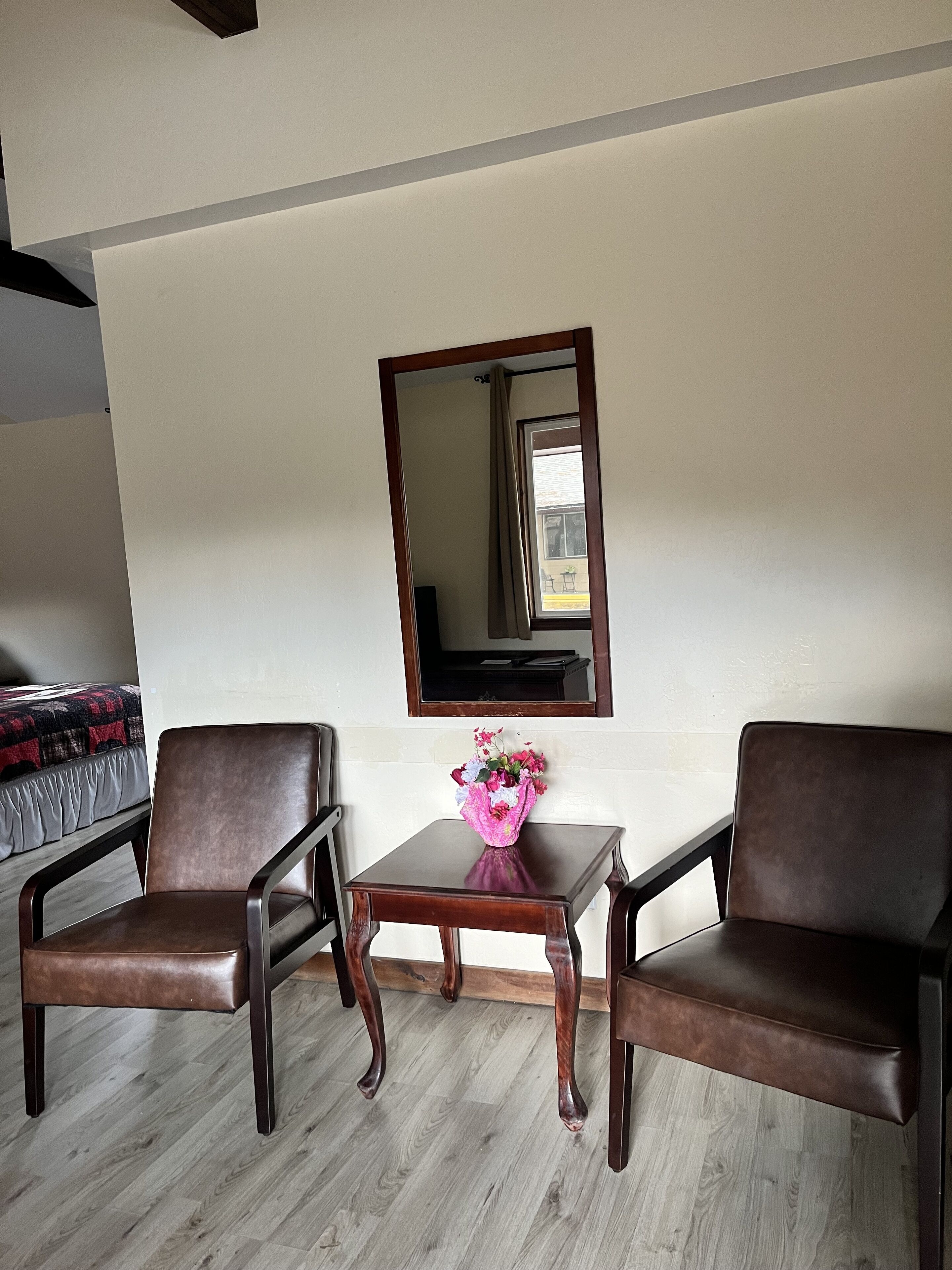 A room with two brown leather chairs, a small wooden table with a vase of flowers, and a mirror on the wall.