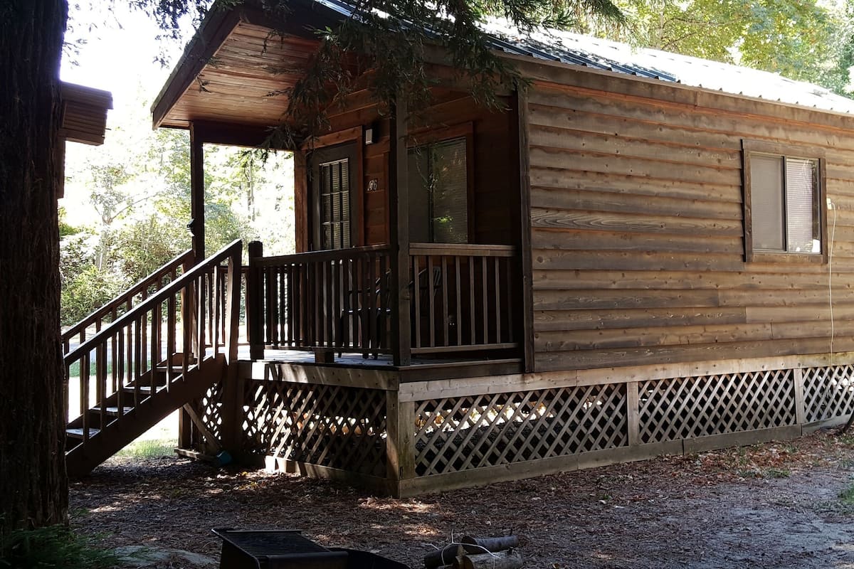 A wooden cabin with a porch, a staircase, and a fenced area.
