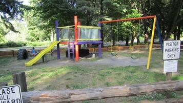 A playground with a slide and swings, surrounded by trees.
