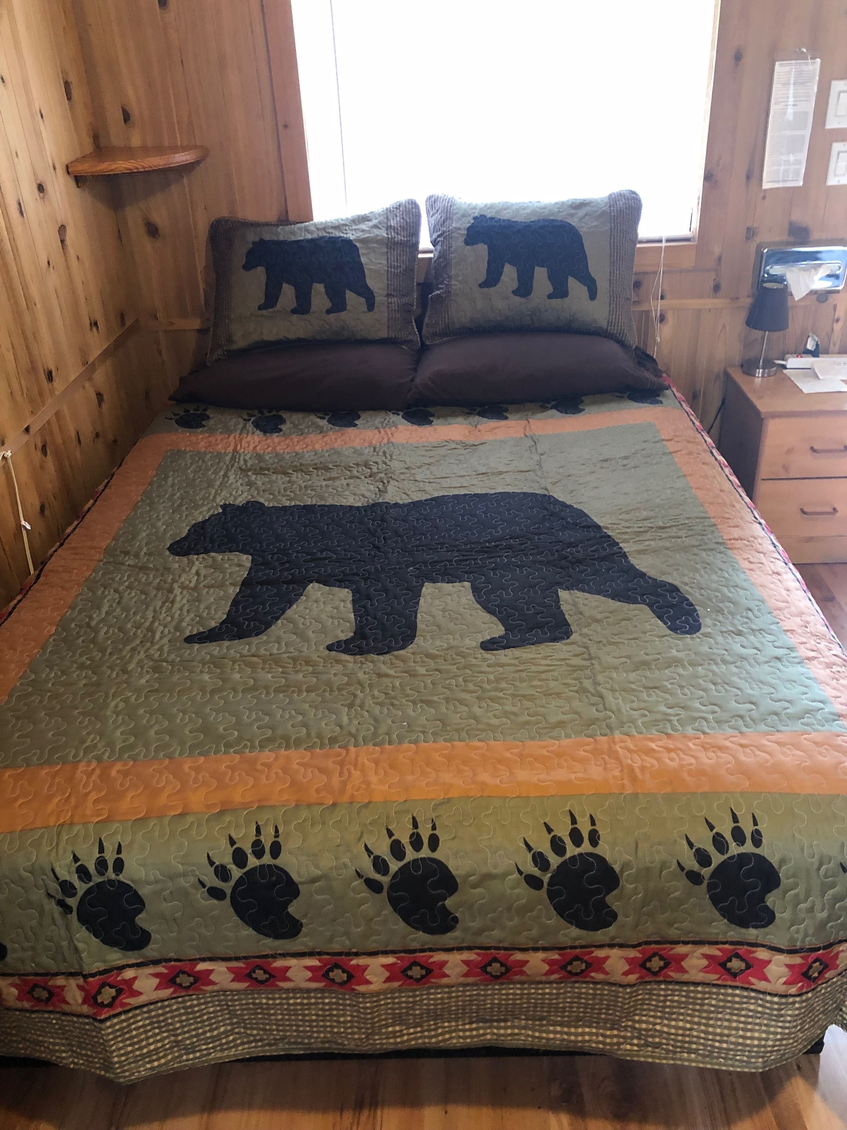 Una cama con colcha de temática de oso, cabecera de madera y mesita de noche con lámpara.