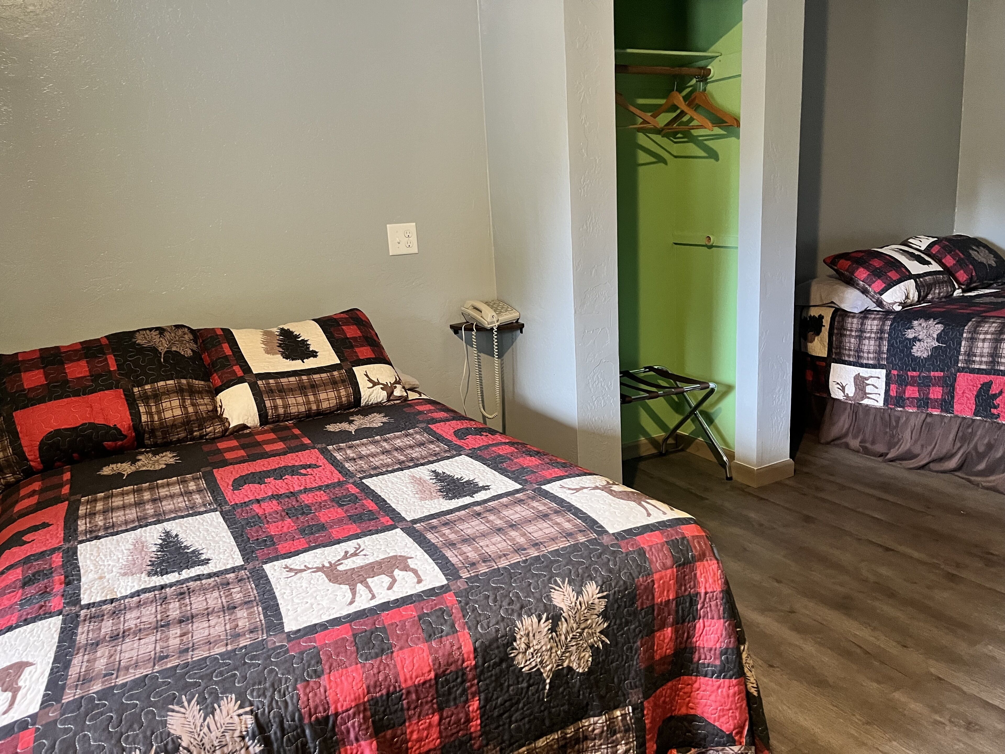 Ein Schlafzimmer mit einem großen Bett, das mit einer rot-schwarzen Steppdecke bezogen ist, einem Nachttisch mit einer Lampe und einer grünen Wand.