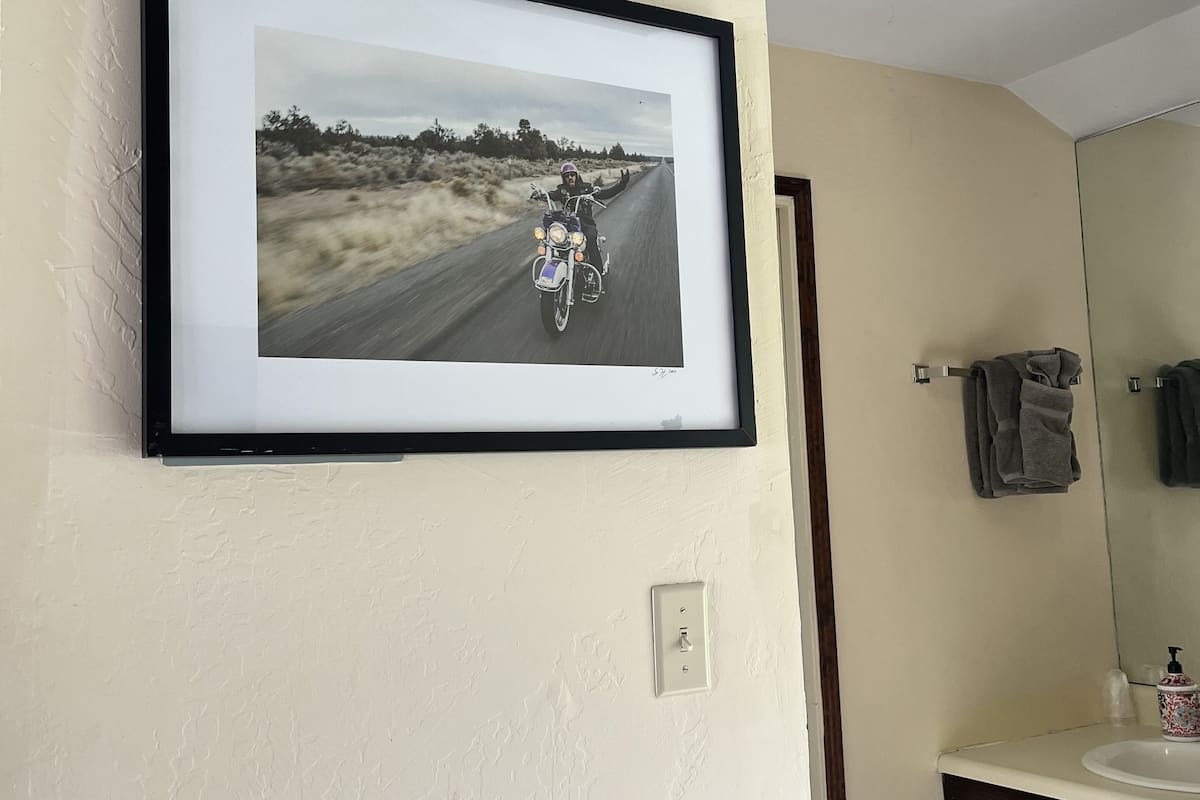 A framed photograph on a wall, a bathroom with a sink and mirror, and a towel rack.