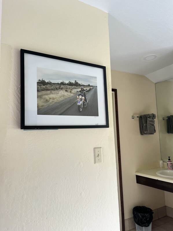 A framed photograph on a wall, a bathroom with a sink and mirror, and a towel rack.