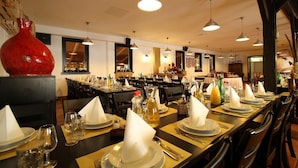Een restaurant met meerdere tafels gedekt voor diner, met een grote rode vaas en hanglampen.