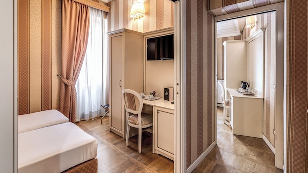 Una camera d'albergo con un letto, una scrivania con sedia, una TV e un armadio.