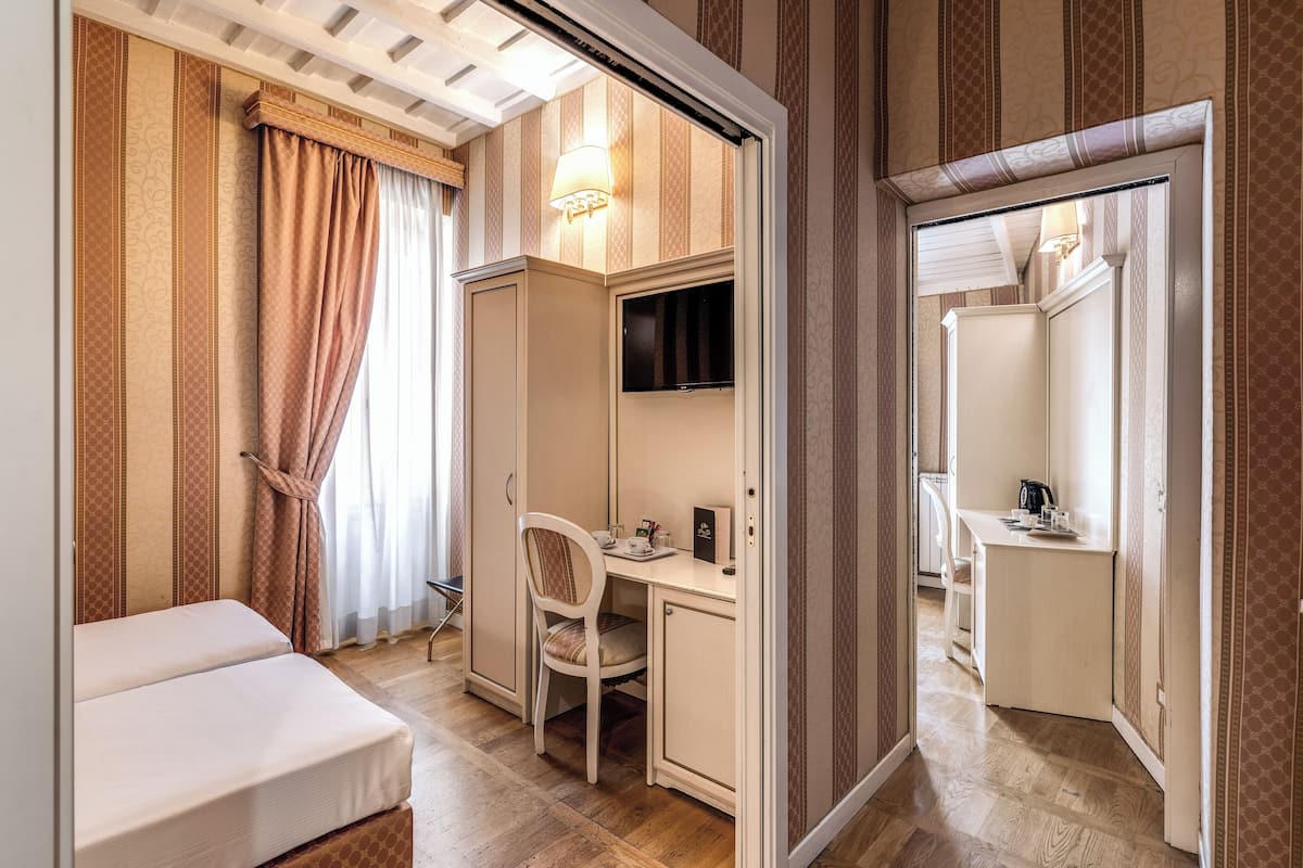 A hotel room with a bed, a desk with a chair, a TV, and a wardrobe.