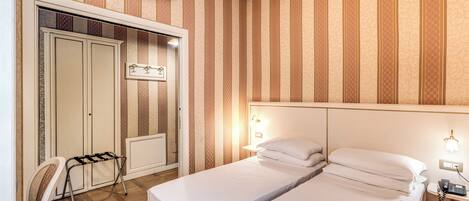 A hotel room with two beds, a wardrobe, a radiator, a chair, and a telephone.