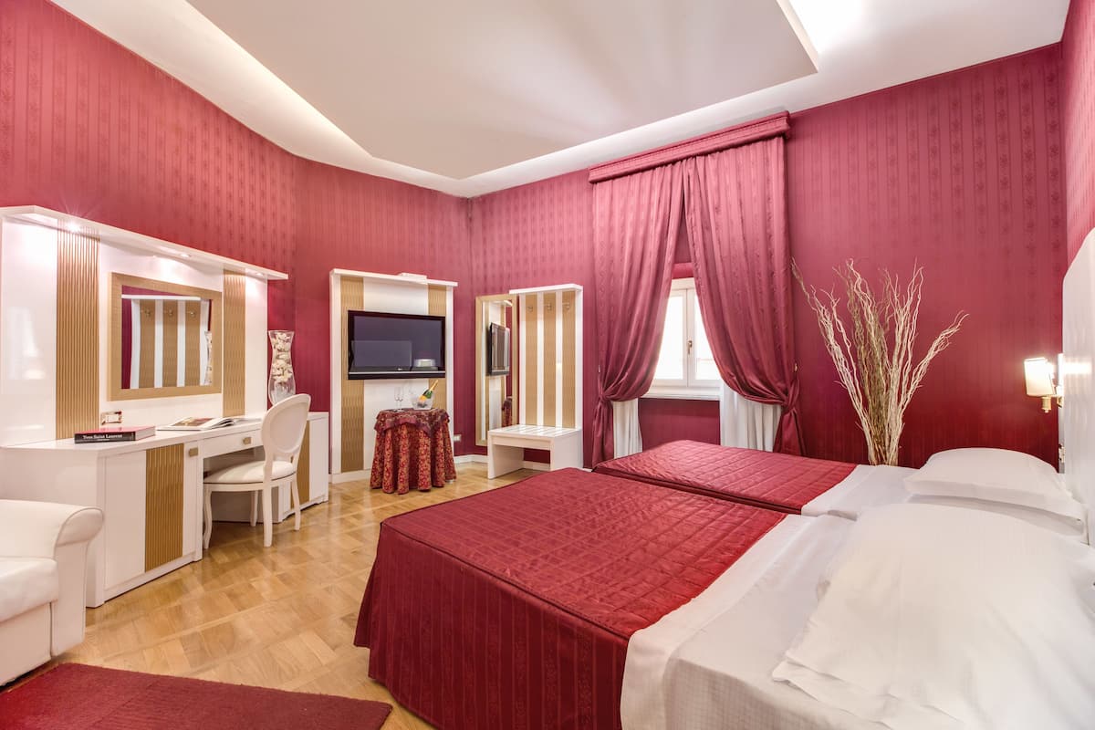 A hotel room with a large bed, a desk, a chair, a TV, and a window with curtains.