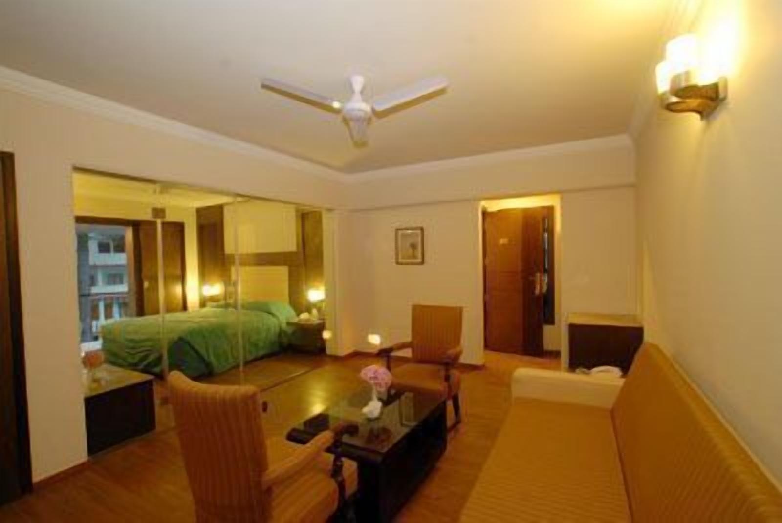 Habitación de hotel con cama, sofá, sillón, mesa de centro y ventilador de techo.