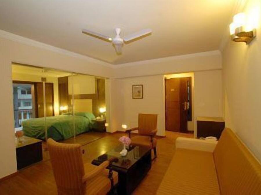 Habitación de hotel con cama, sofá, sillón, mesa de centro y ventilador de techo.