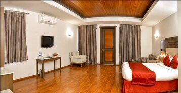 A hotel room with a wooden ceiling, a bed with red bedding, a desk with a television, and a chair.