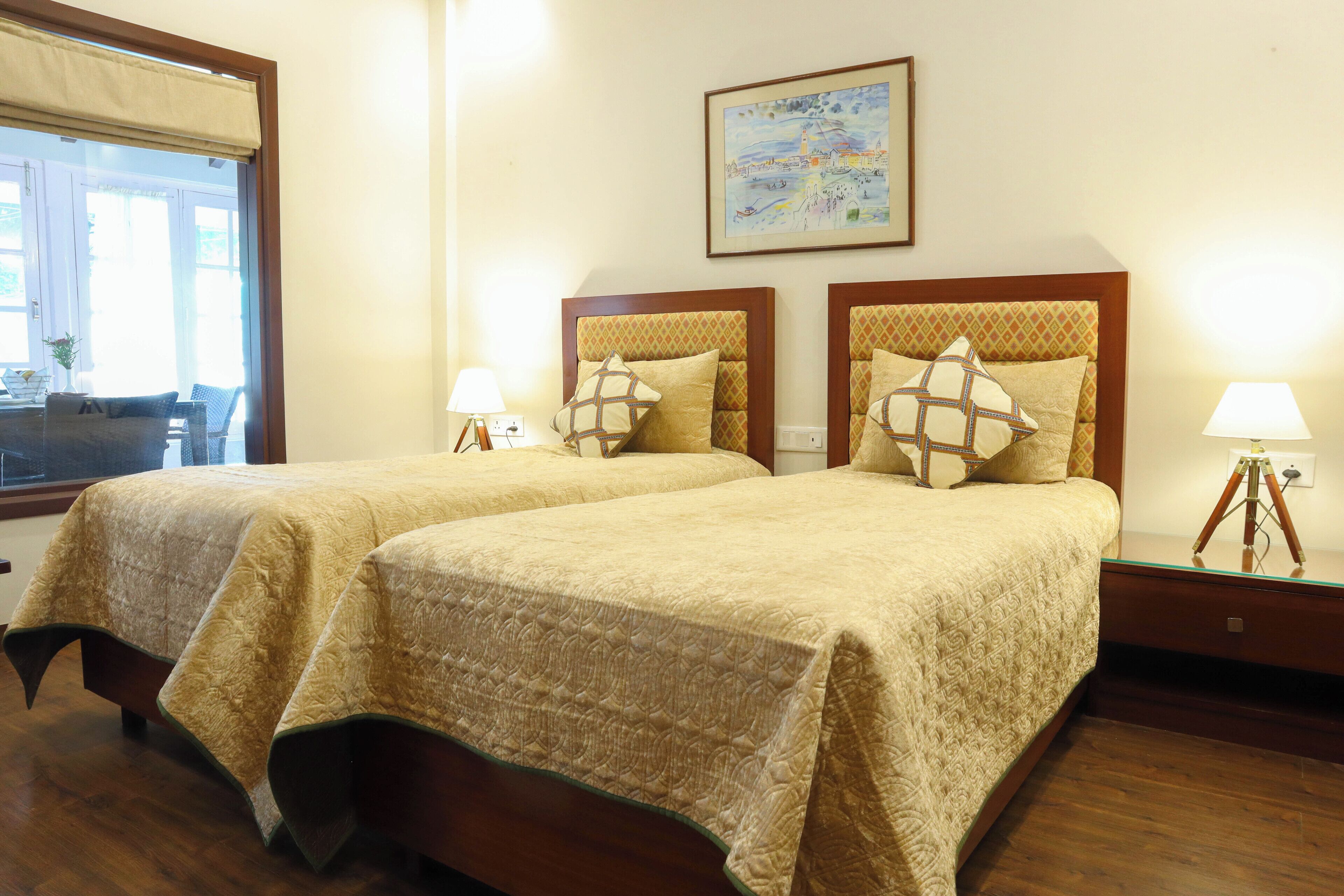 Habitación de hotel con dos camas, cada una con una colcha estampada y almohadas a juego. Hay una ventana con vistas al exterior, un cuadro en la pared y una mesita con una lámpara.