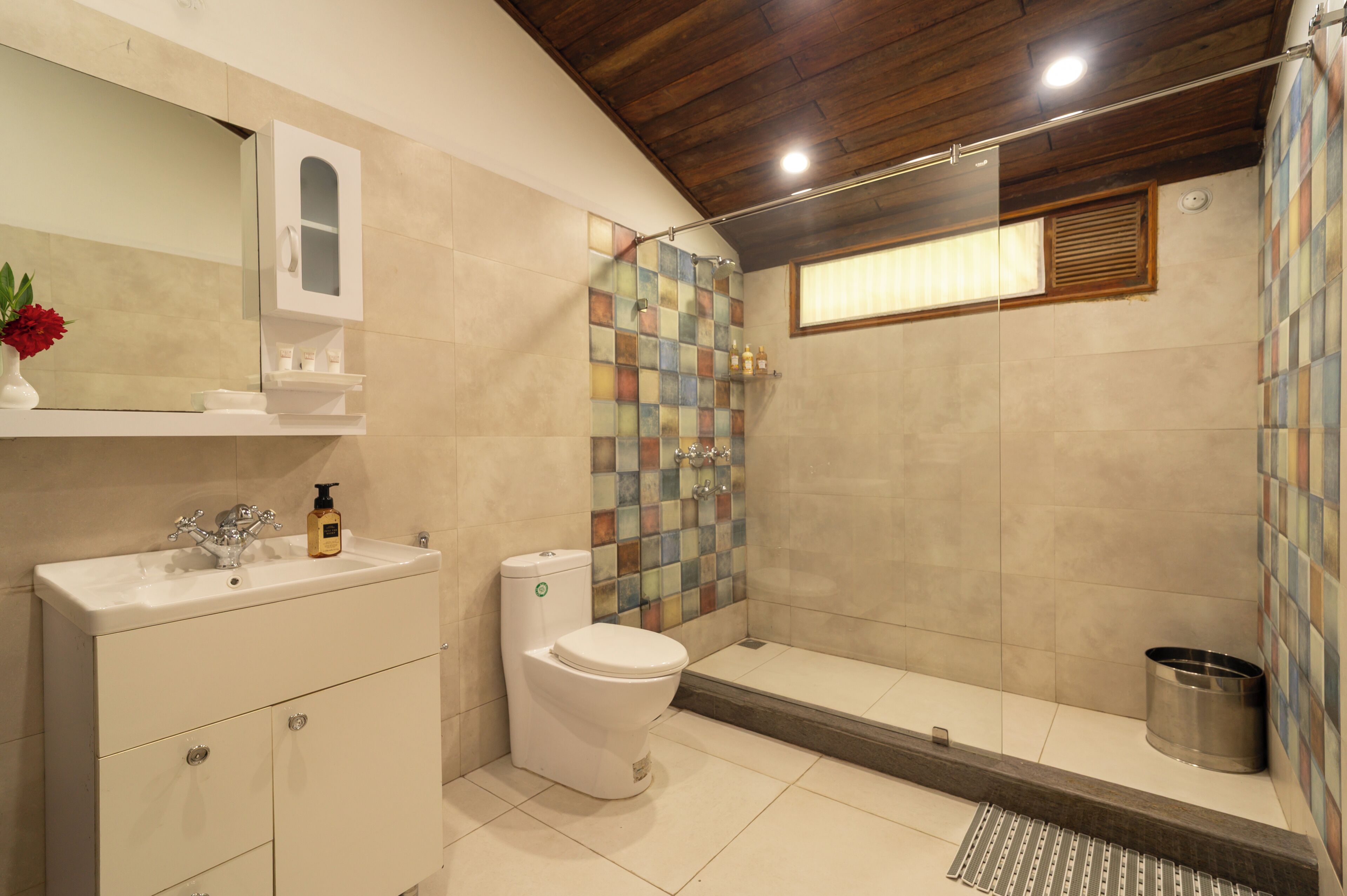 Bany amb un rentatge blanc, un vàter, una dutxa amb un mur d'azulejos i un sostre de fusta.