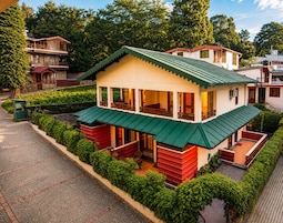 A two-story building with a green roof, surrounded by greenery and a paved area.