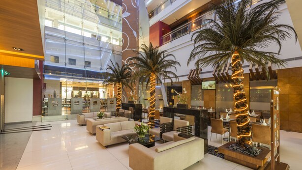 A spacious lobby with multiple seating areas, palm trees, and a modern interior design. - The Regenza by Tunga (Navi Mumbai)