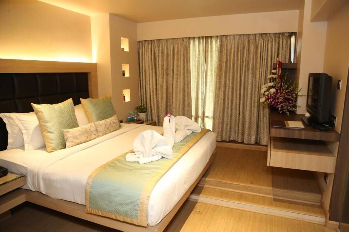 A hotel room with a bed, a TV, a desk, and a large window with curtains.