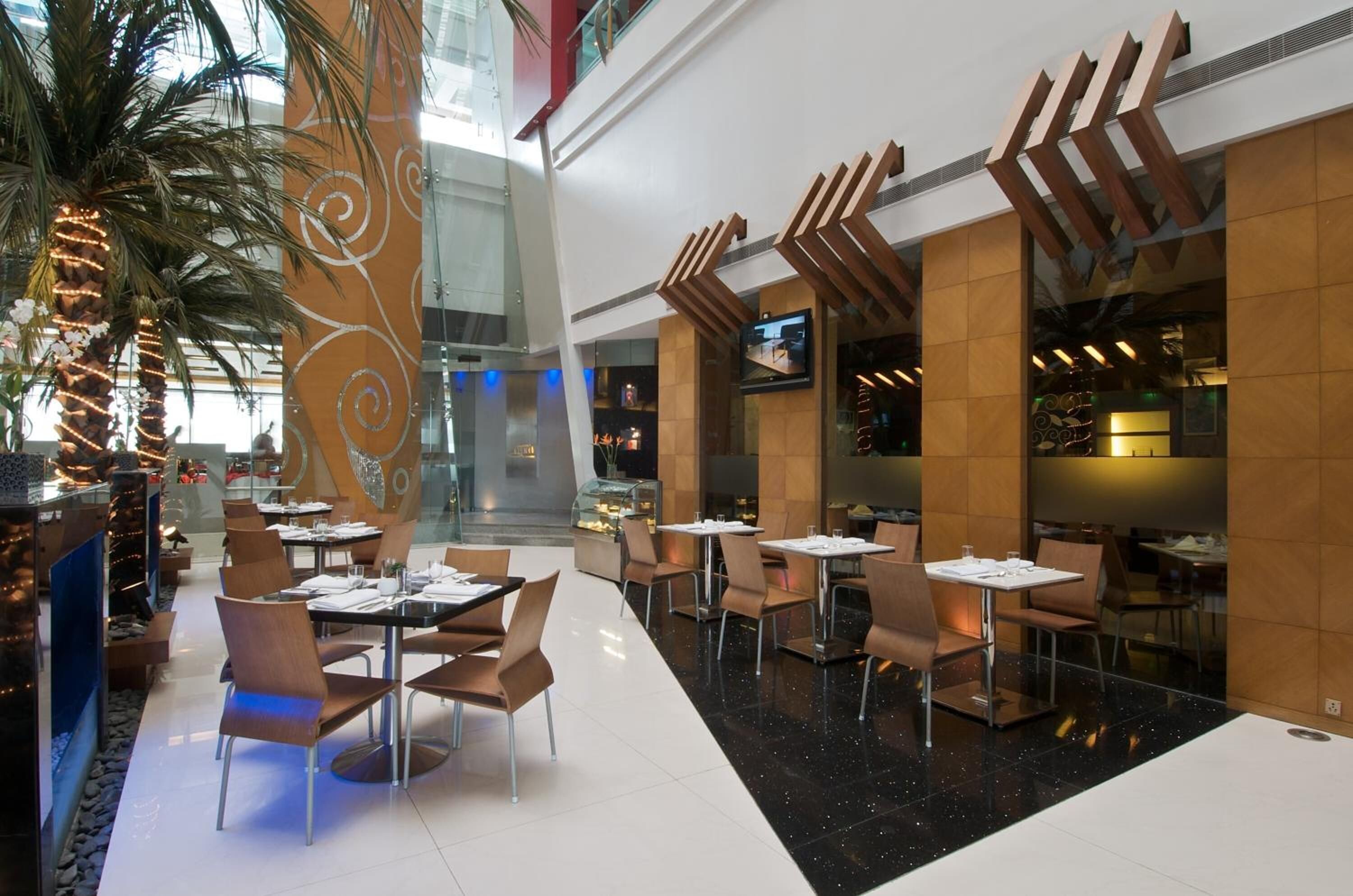 Un restaurante moderno con techos altos y un atrio central. Mesas y sillas dispuestas para comer.