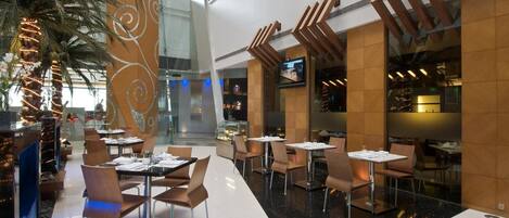 A modern restaurant with high ceilings and a central atrium. Tables and chairs are arranged for dining.