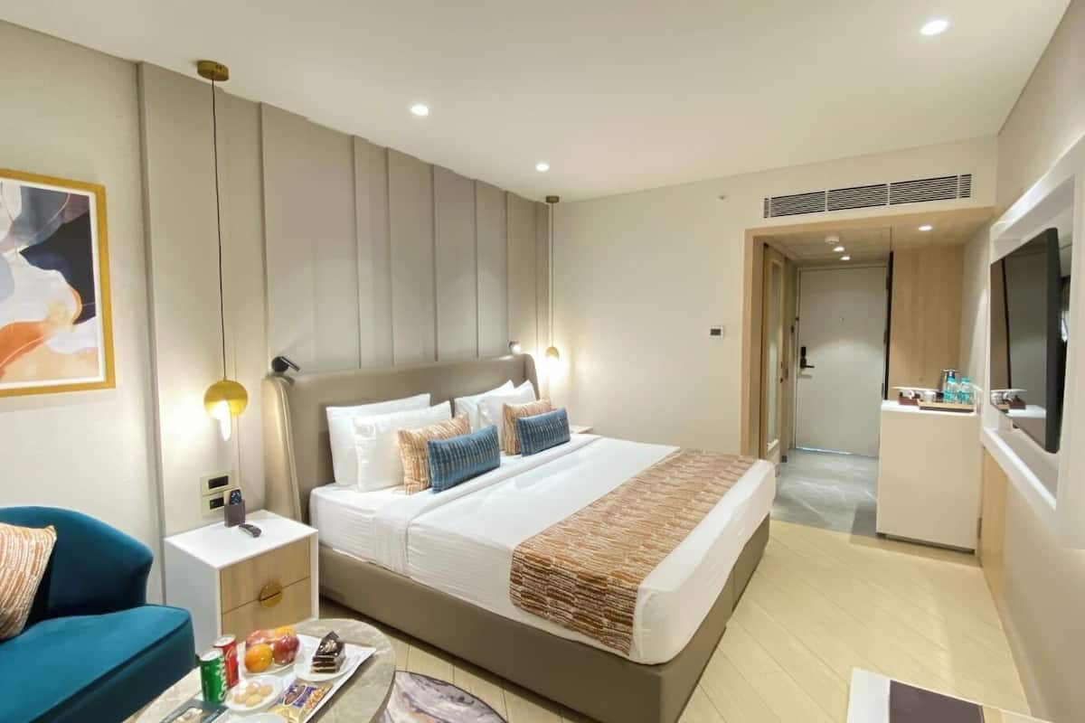A modern hotel room with a large bed, bedside tables, a desk, a chair, and a TV.