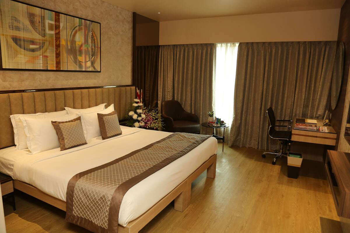 A hotel room with a large bed, a desk, a chair, and a large window with curtains.