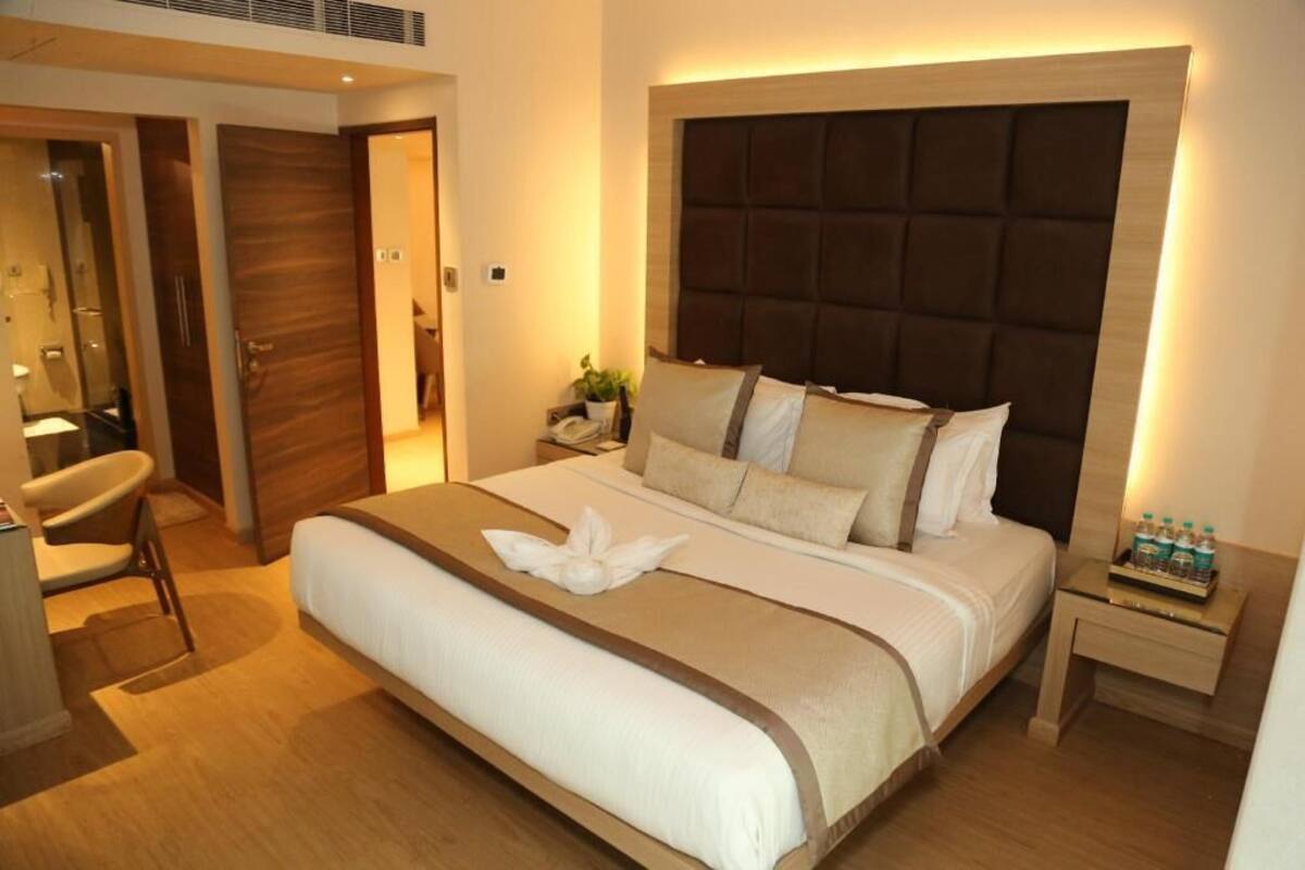 A hotel room with a large bed, a bedside table with water bottles, and a chair.