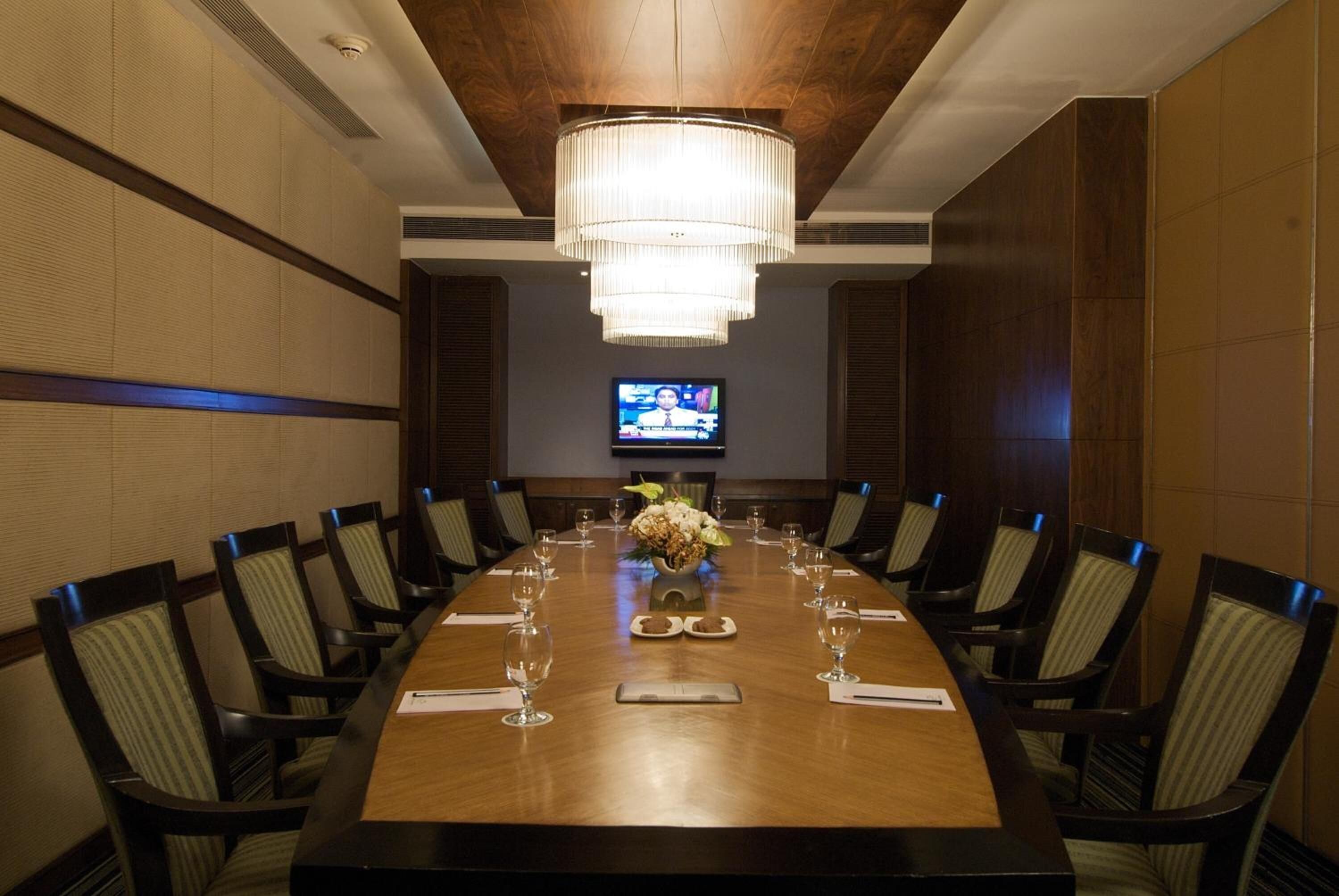 A conference room with a long table, chairs, a chandelier, a television, and a floral centerpiece.
