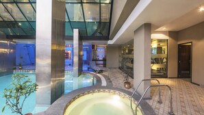 An indoor swimming pool with a glass ceiling, a lounge area with a chair, and a view of the sky. - The Regenza by Tunga (Navi Mumbai)