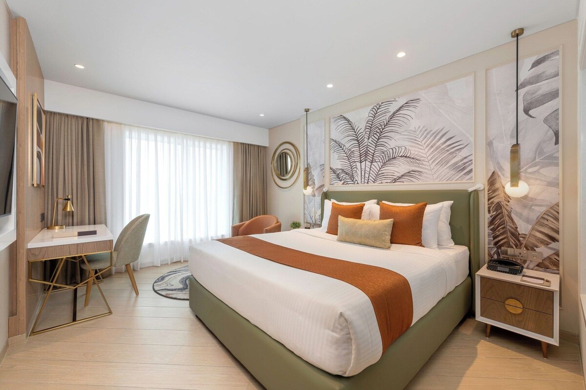 A hotel room with a large bed, a desk, a chair, and a TV.