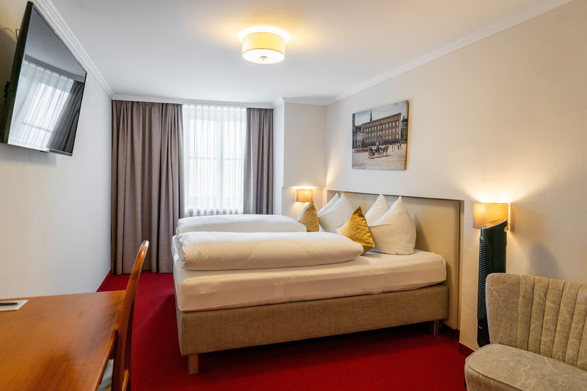 Ein Hotelzimmer mit einem großen Bett, zwei Nachttischlampen, einem Flachbildfernseher, einem roten Teppich und einem gerahmten Bild an der Wand.