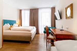 Habitación de hotel con cama, escritorio, silla, televisión y ventana con cortinas.