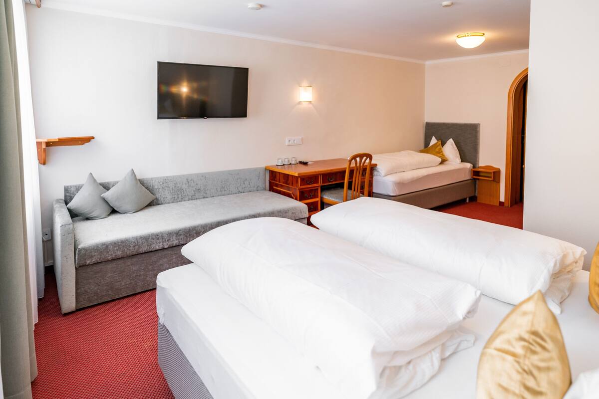 Ein Hotelzimmer mit einer Couch, zwei Einzelbetten, einem Schreibtisch und einem Fernseher.