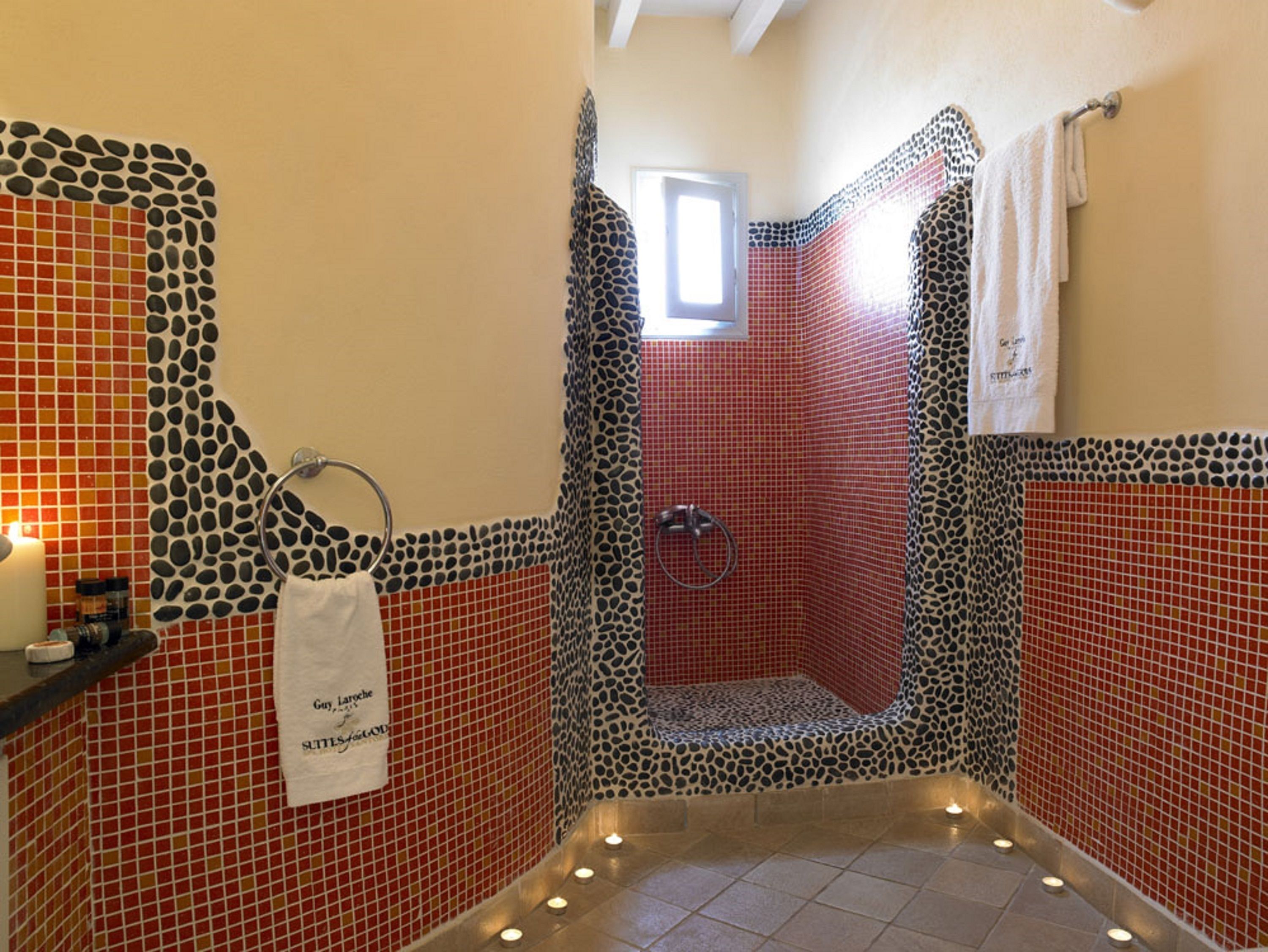 Bagno con zona doccia, pareti e pavimento in mosaico, un porta asciugamani e una piccola finestra.