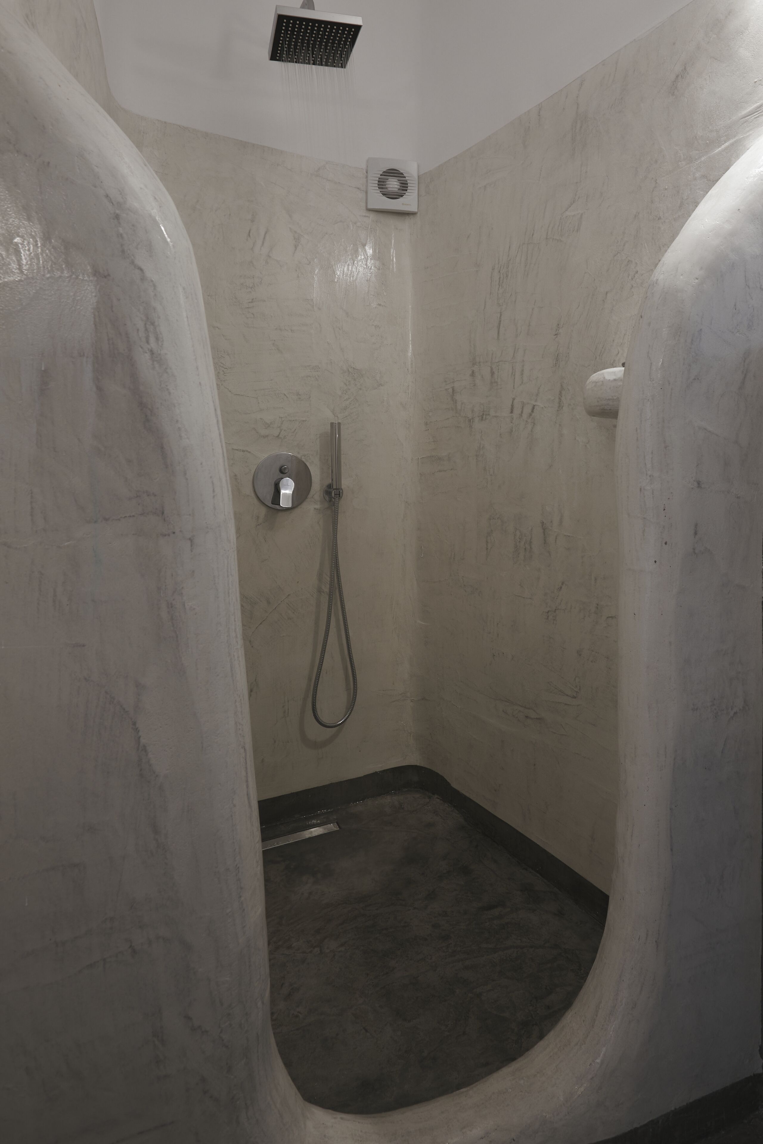 A shower area with a handheld showerhead, a wall-mounted control, and a floor drain.