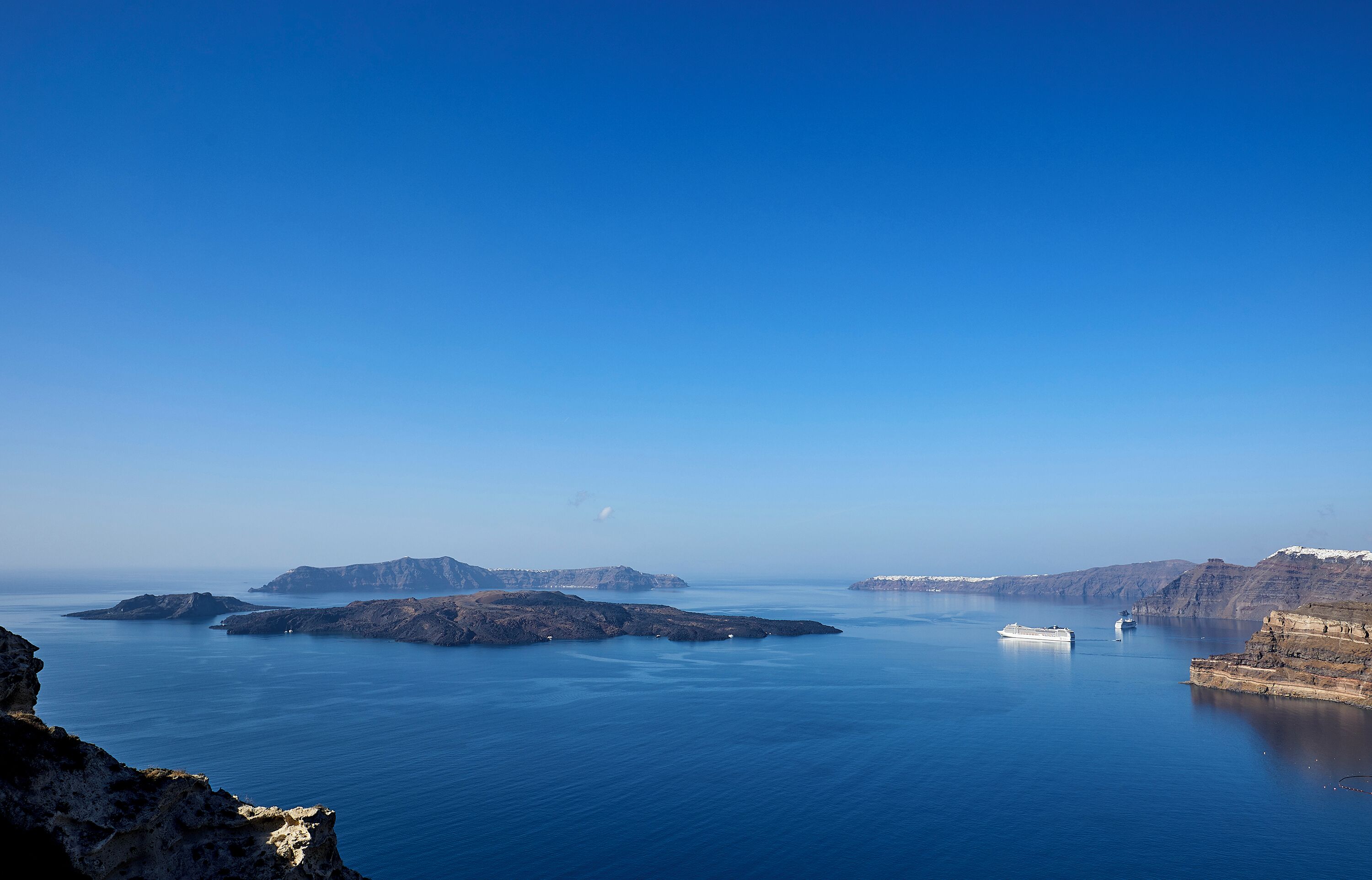 A coastal landscape with clear blue waters, rocky outcrops, and a boat in the distance.