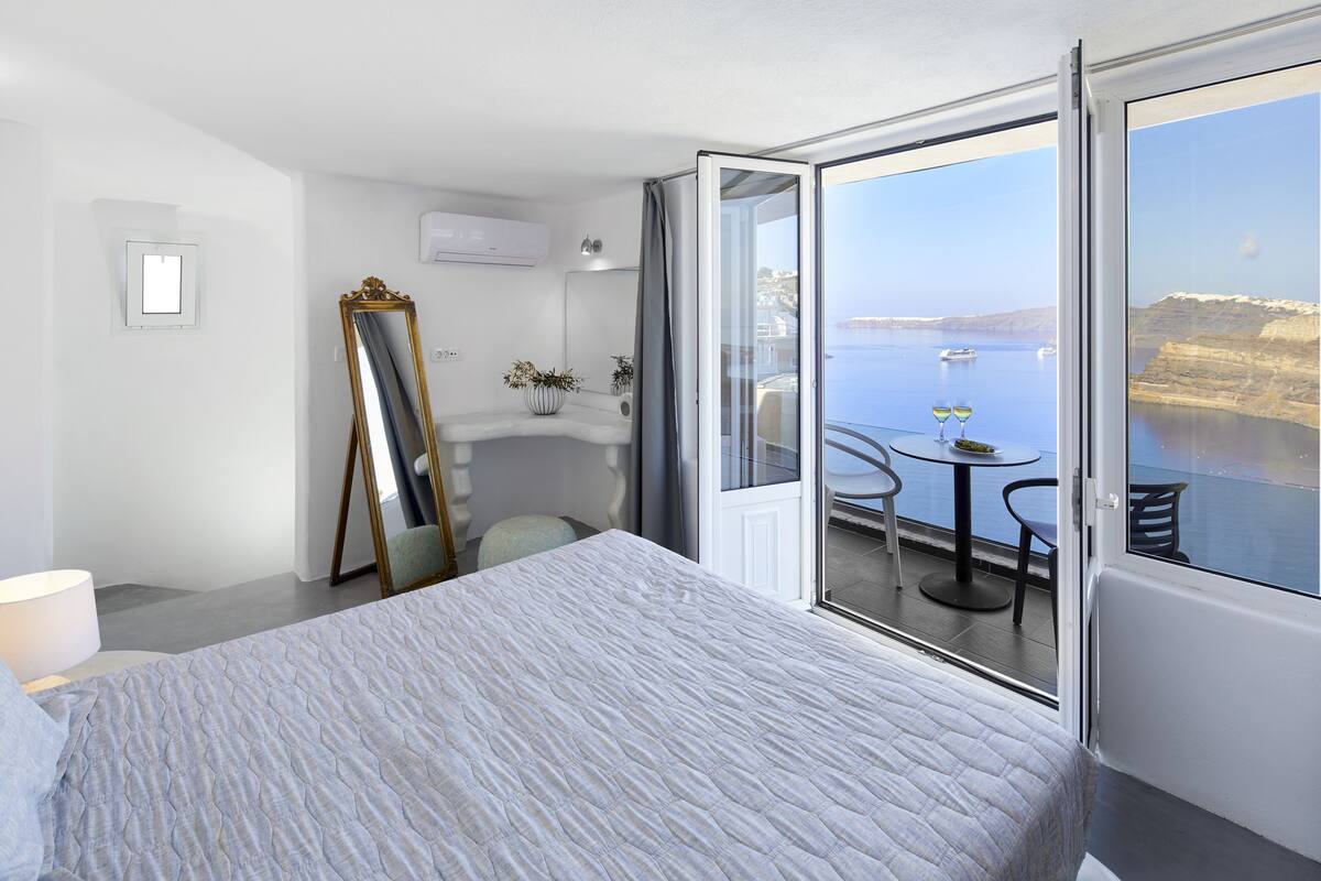 Une chambre à coucher avec un grand lit, un miroir et un balcon doté d’une table et de chaises, donnant sur une étendue d’eau.
