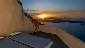 Una habitación iluminada por el sol con vista al atardecer sobre el agua, que incluye dos camas y suelo de piedra.