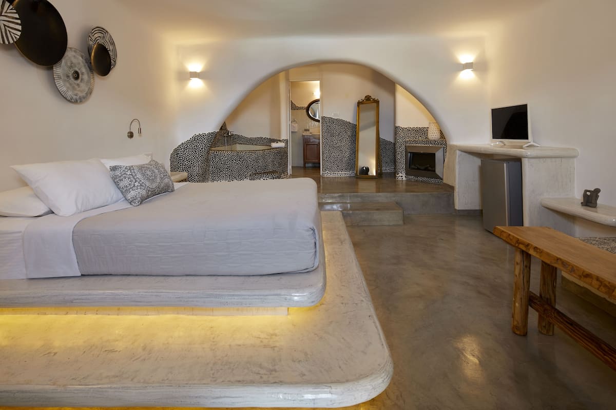 Une chambre moderne avec un grand lit, un banc en bois et un bureau avec un ordinateur.
