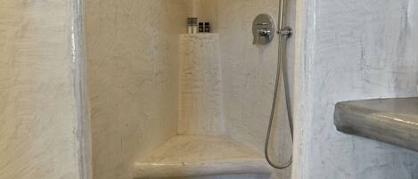A bathroom with a shower, marble walls, and a showerhead.