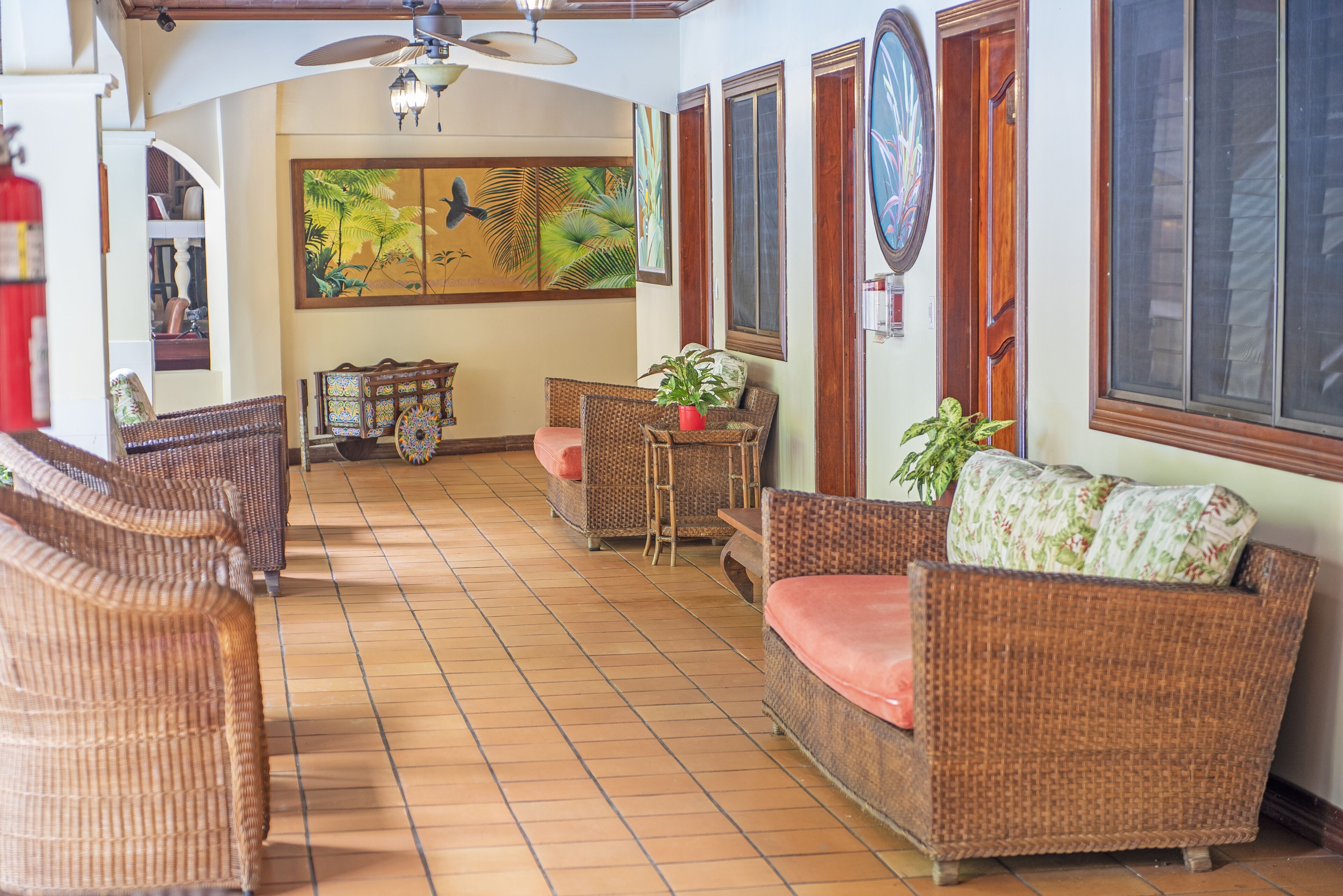 A spacious living area with wicker furniture, a tiled floor, and a large painting on the wall.