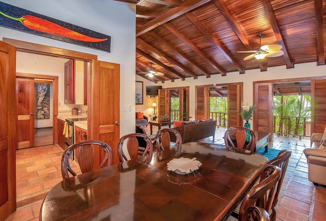 A spacious dining area with a wooden table and chairs, a ceiling fan, and a view of the outdoors.
