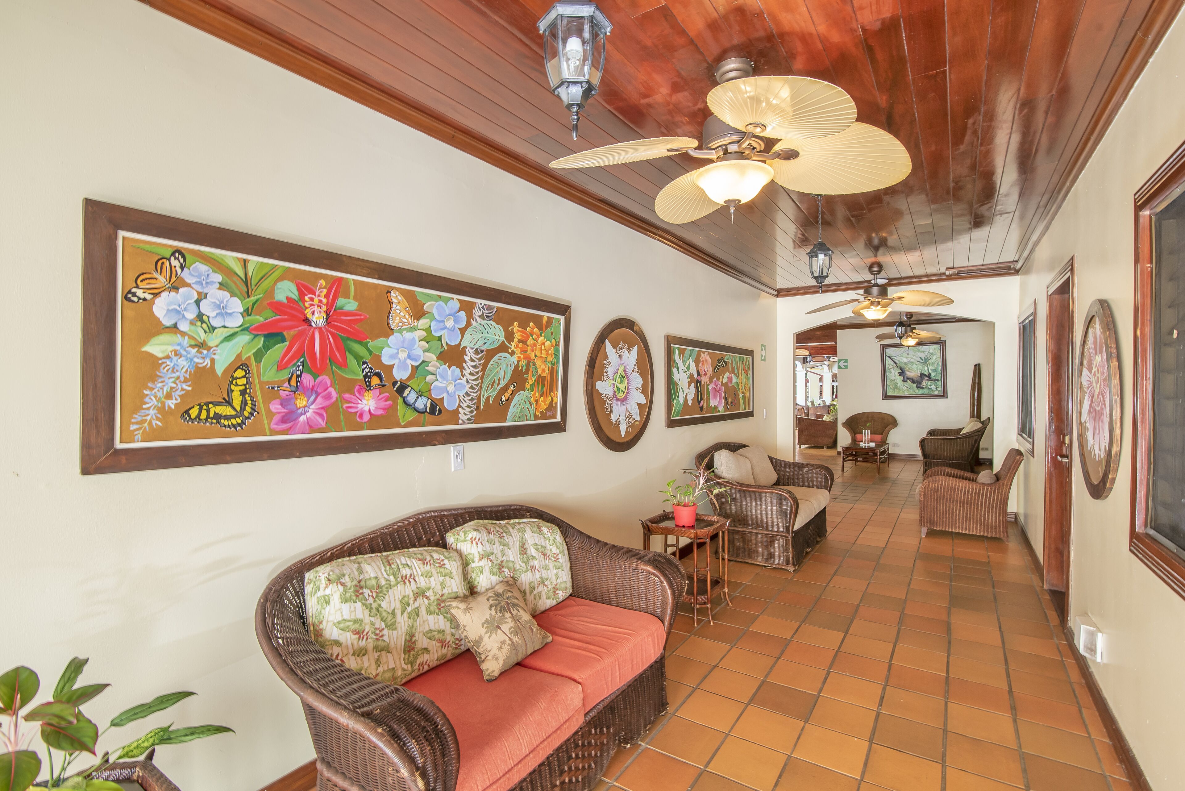 Amplia sala de estar con un cuadro grande de flores, muebles de mimbre y piso de baldosas.