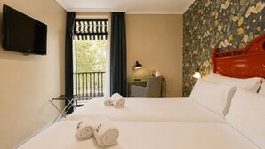 A hotel room with two beds, a TV, a balcony with a view, and a patterned wallpaper. - Petit Palace Puerta de Triana (Seville)