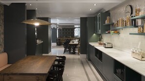 A modern kitchen with dark cabinetry, a wooden dining table, and a hanging light fixture. - Petit Palace Puerta de Triana (Seville)