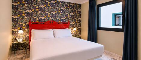 A hotel room with a bed, floral wallpaper, a red headboard, two bedside lamps, a window with curtains, and a marble floor.