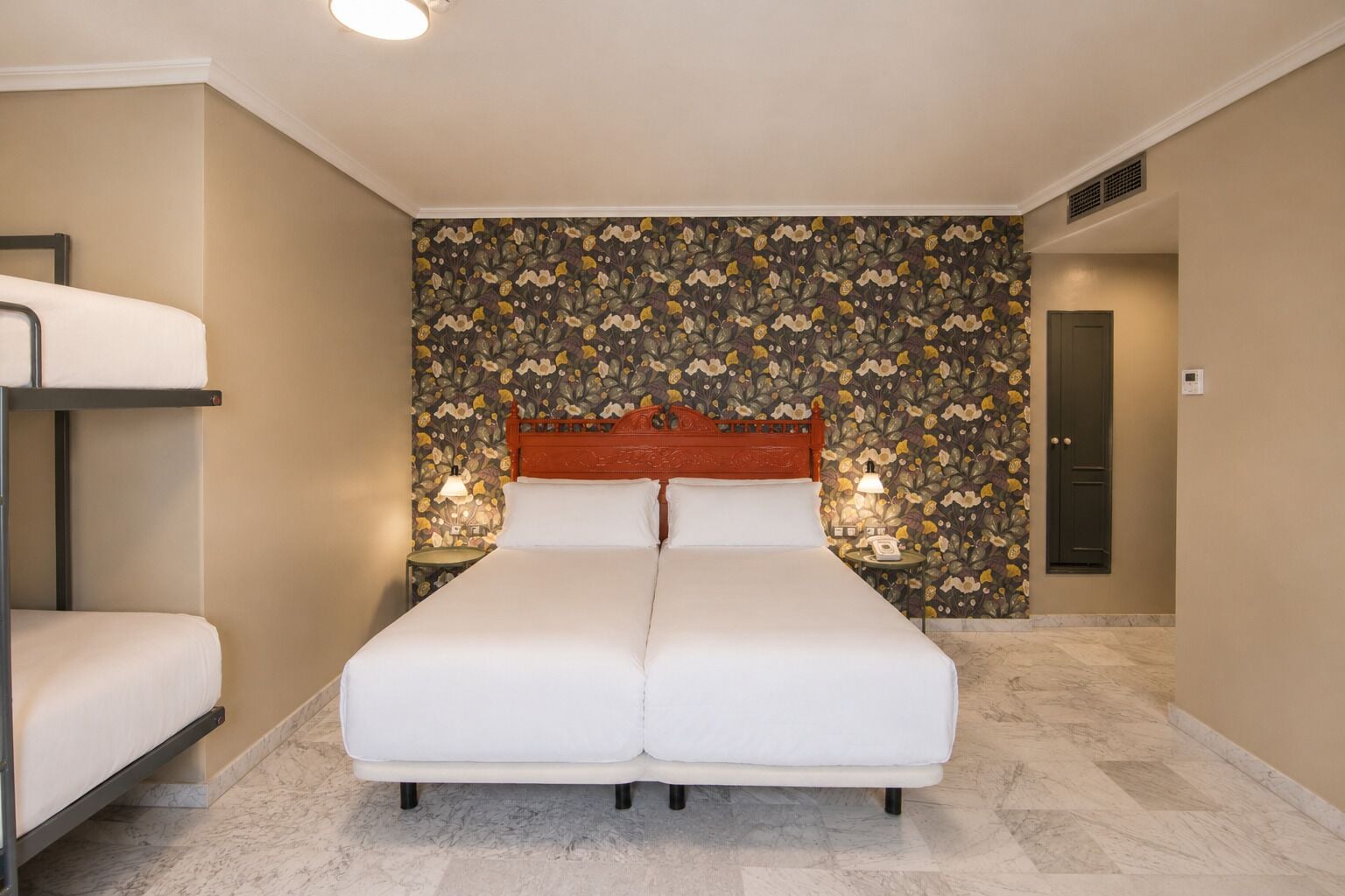 A hotel room with a bed, a nightstand, a lamp, a wardrobe, and a bunk bed.