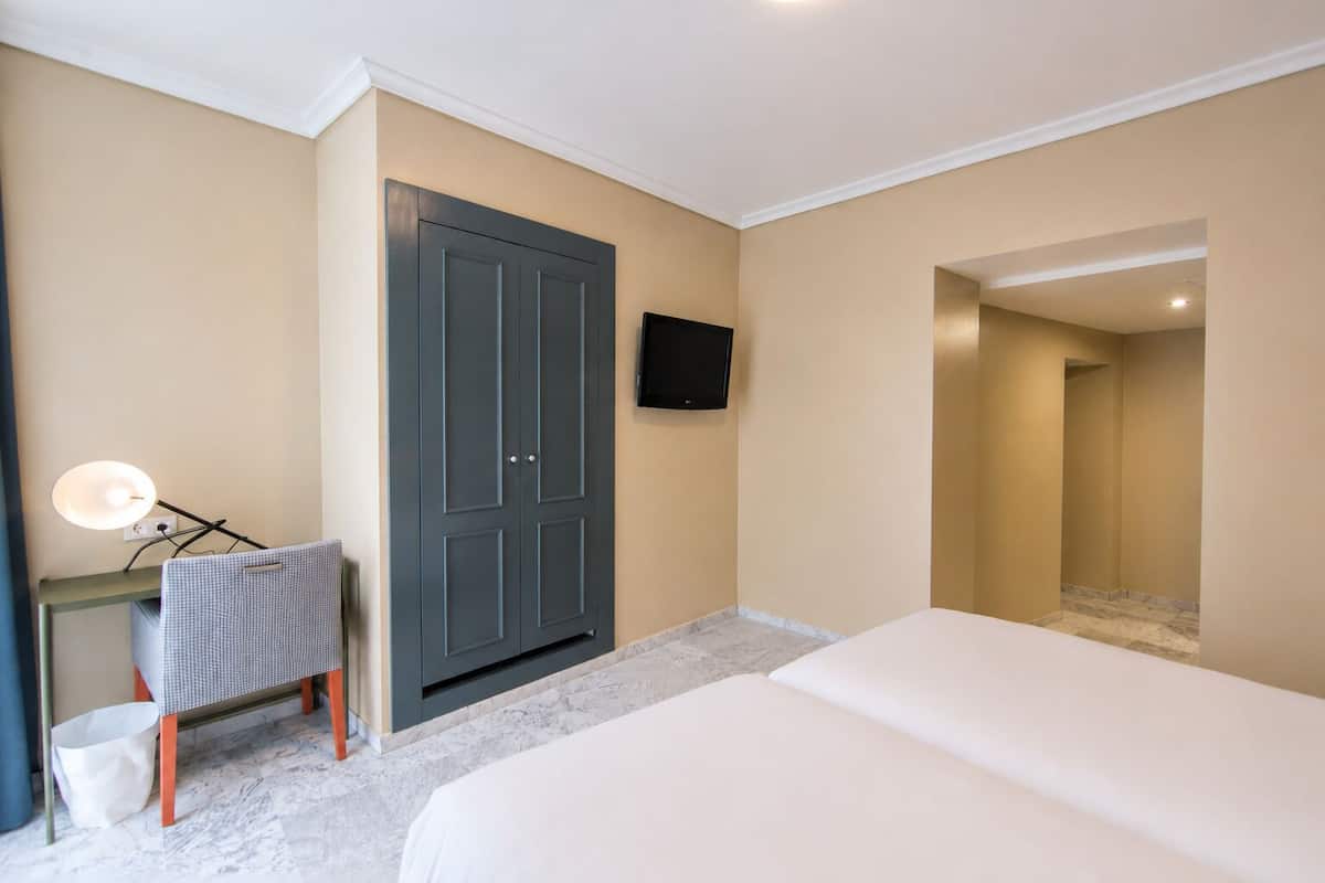 Une chambre d’hôtel comprenant un lit, un bureau avec une lampe, une armoire et un téléviseur fixé au mur.