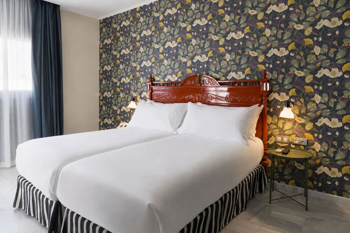 Un lit double avec une tête de lit en bois, une literie blanche, une jupe de lit à rayures et un papier peint à motifs floraux.