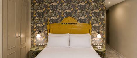 A hotel room with a large bed, floral wallpaper, a yellow headboard, two bedside lamps, and a marble floor.